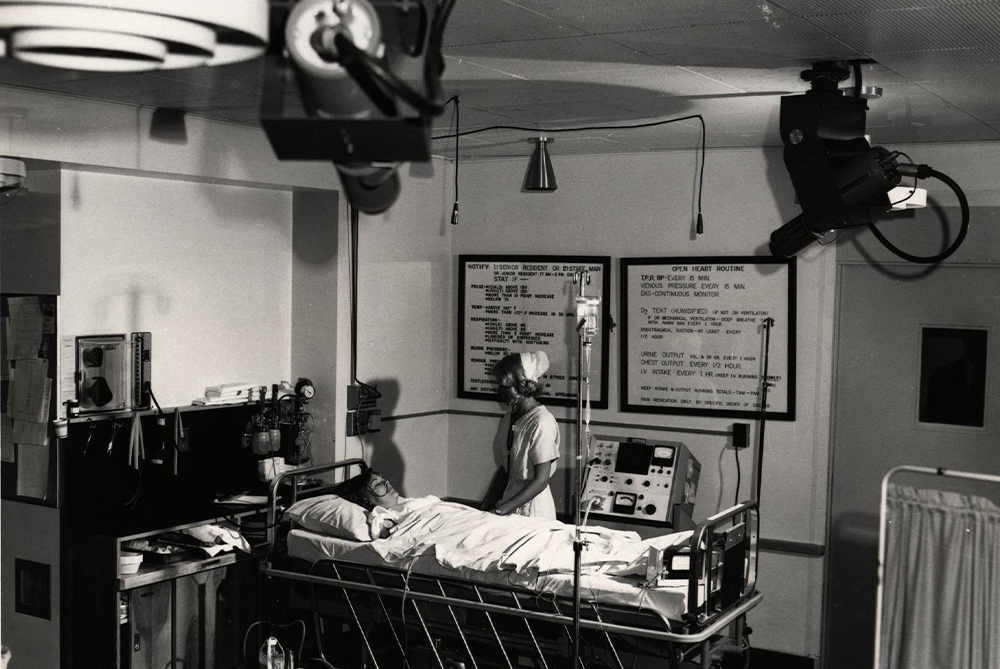 A nurse cares for a patient after open-heart surgery with cameras recording her care mounted on the ceiling
