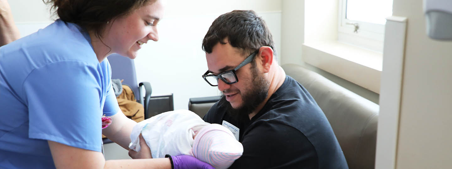 BSN student Elissa Hoyt hands baby Ayla to new father Kevin Sanabria, as mother Alondra looks on off camera. 